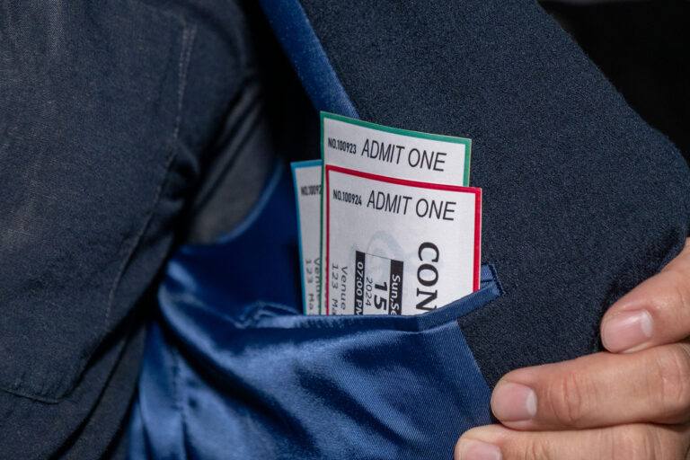 A hand extracts three concert tickets from a pocket, a common tactic used in ticket scalping